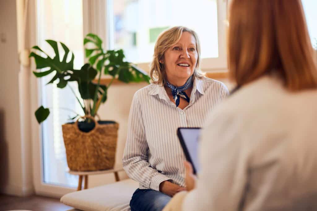 Older woman smiling during a therapy session with a counselor in a bright room.