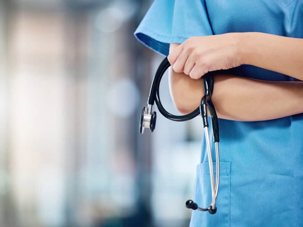 Nurse in scrubs holding a stethoscope in a medical setting.